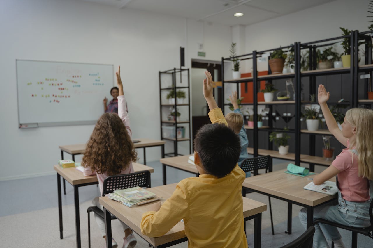 digital Diverse group of students raising hands in a vibrant classroom setting with teacher at front.