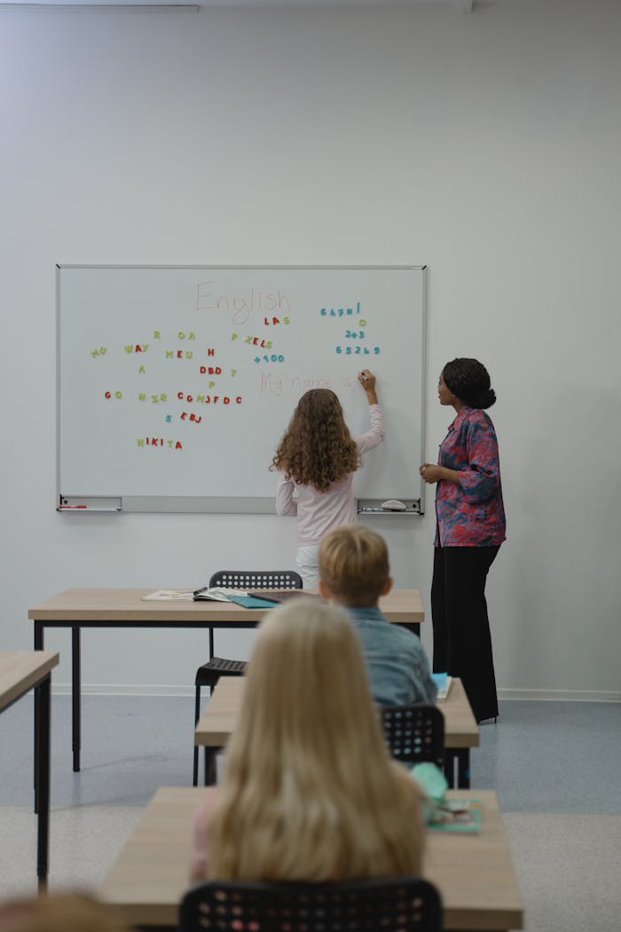 Teacher instructing diverse students with magnetic letters on a classroom whiteboard.
