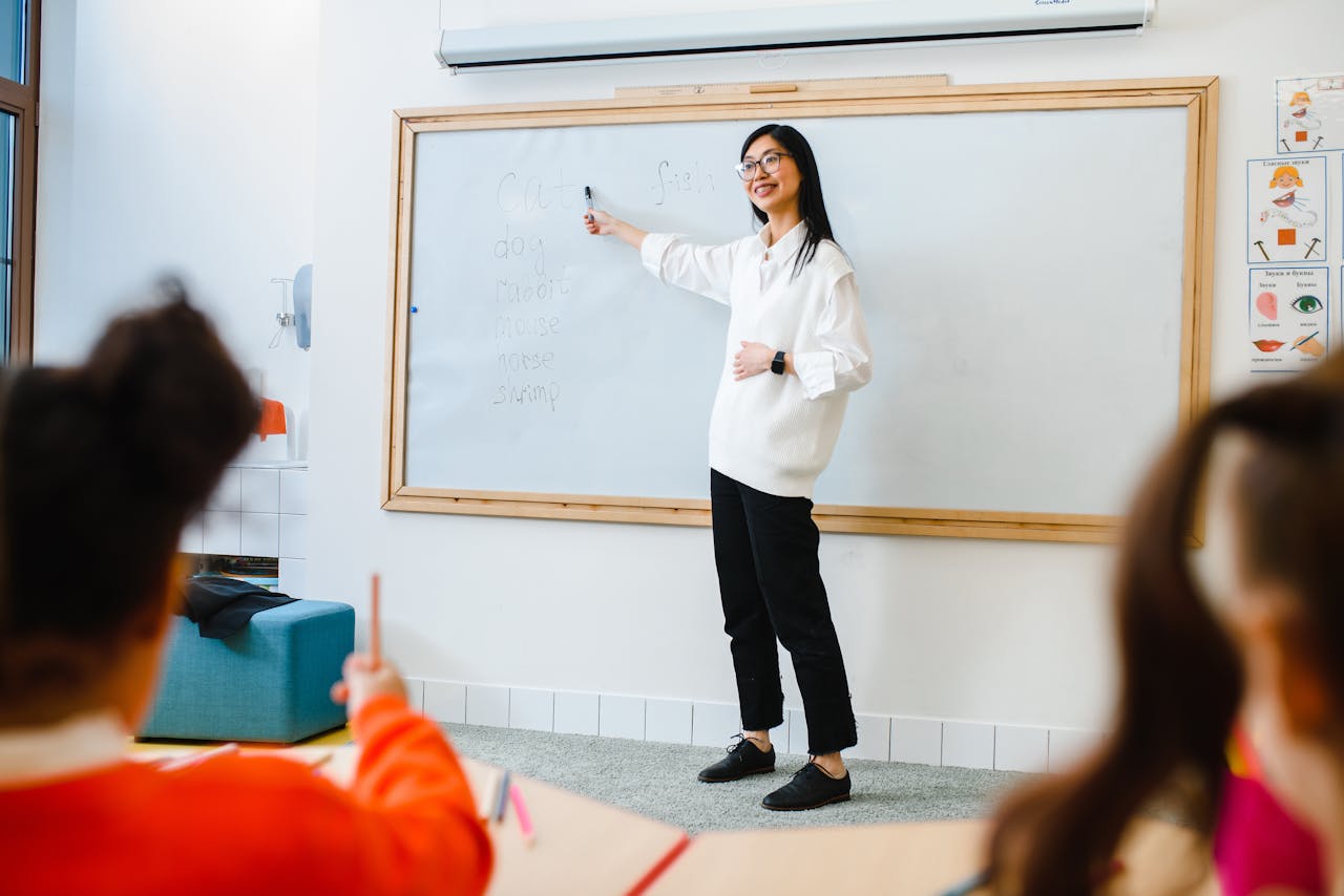 Services-01 Smiling teacher instructing students in a classroom setting using a whiteboard.